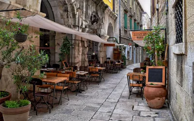 Gost rezervira stol u restoranu putem mobitela dok sjedi na terasi apartmana, simbolizirajući online rezervaciju u turističkoj destinaciji.